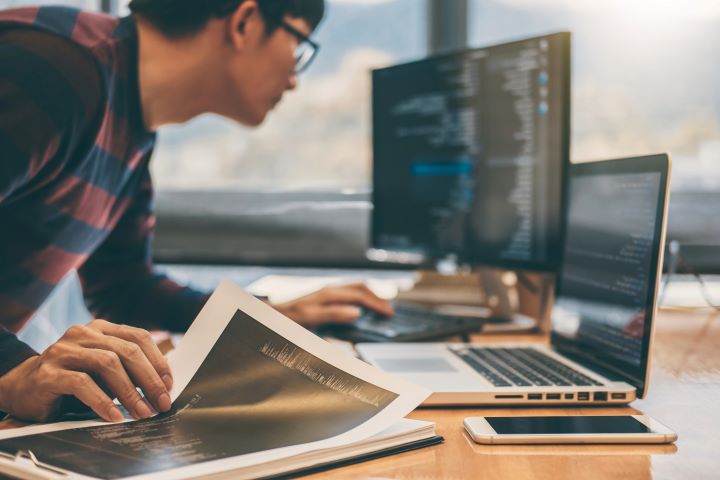 Ein Mann sitzt vor einem Laptop und einem Papier, während er an der Migration nach Microsoft SharePoint oder Office 365 arbeitet.